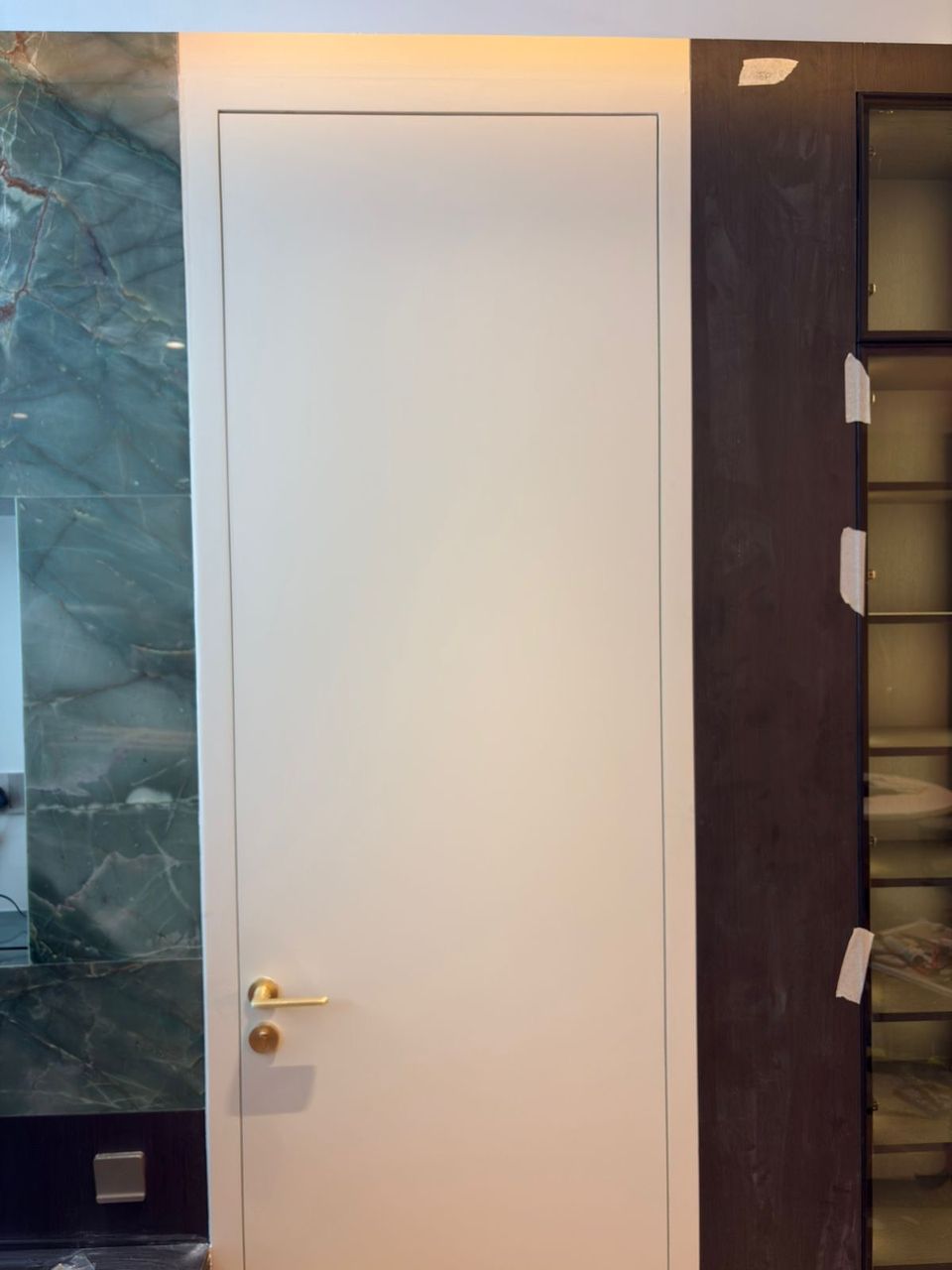 White Flush Door With Brass Lever Beside Marble